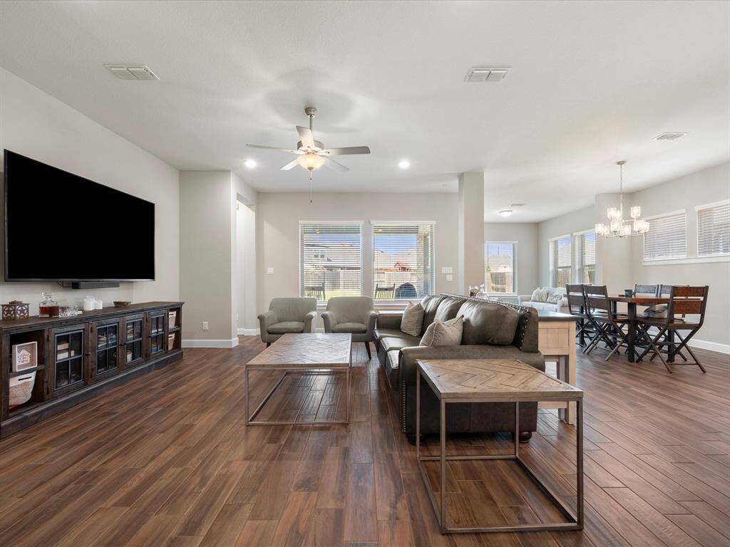 Expansive open-concept living and dining area, enhanced by gleaming wood-look tile flooring, serene neutral tones, and an abundance of natural light. The living room offers generous space for your furnishings, complemented by a sleek contemporary ceiling fan that elevates the sophisticated ambiance. Seamlessly connected, the dining area comfortably accommodates a table of 6-8 beneath a stylish chandelier, adding a refined touch of modern elegance.