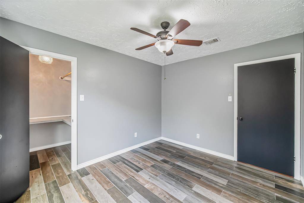 This angle of the third of three bedrooms shows tile flooring, a ceiling fan, and a walk-in closet that could be used as a small office or craft area.