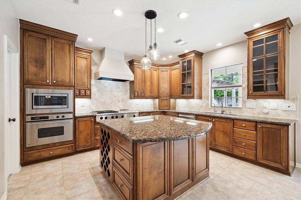 The gourmet kitchen boasts extensive cabinetry, an oversized built-in stainless steel refrigerator, and a professional grade gas cooktop with gas burners, a griddle, and grill. Granite countertops and a timeless backsplash complete the elegant design.