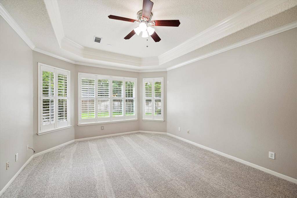 Located on the first floor, the expansive primary suite offers a tranquil retreat, complete with new carpet and a sitting area positioned in front of large windows adorned with plantation shutters. A tray ceiling with crown molding adds architectural interest and enhances the room's ambiance.