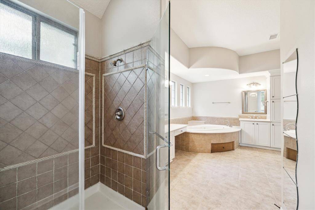 Dual sinks with framed mirrors and a separate vanity complete the functionality and elegance of the primary bathroom. A generously sized walk-in shower is discreetly positioned for added privacy.