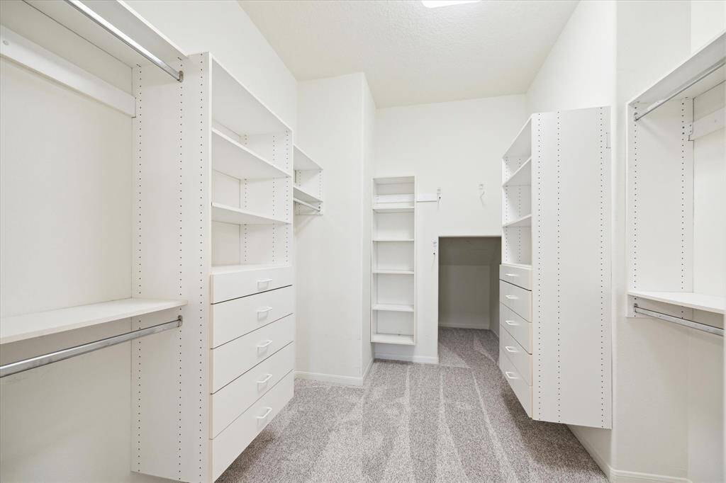 The large primary walk-in closet features two rows of hanging space, providing ample room for organization. High ceilings add to the open feel, while shelving and drawers on both sides offer additional storage options for an organized space!