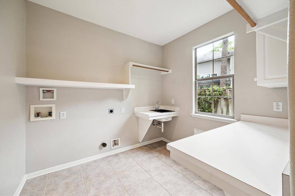 This generously sized laundry room is equipped with a large window that allows for plenty of natural light. It includes convenient folding space, hanging racks, and a sink, making it a functional and organized area.