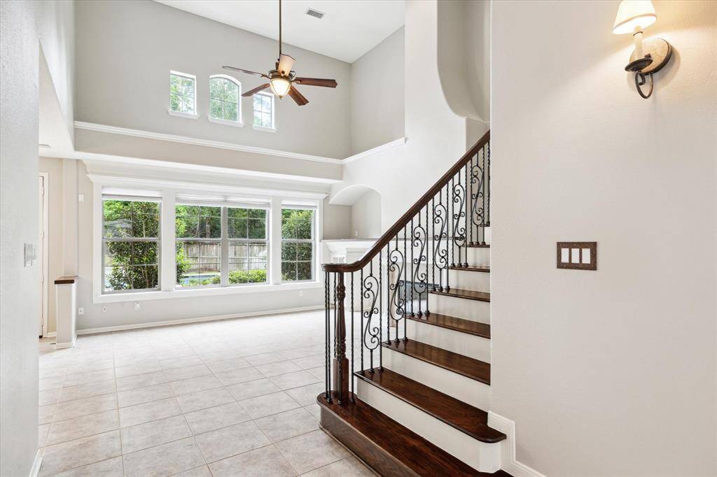 Beyond the entryway, the home opens up to a soaring living area with high ceilings and a striking staircase featuring rich engineered wood flooring.