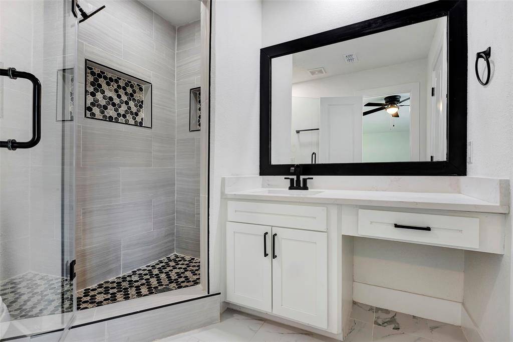 The primary bathroom mirrors the secondary bathroom, featuring a glass-enclosed shower, single sink, and a vanity mirror for a clean and functional space.