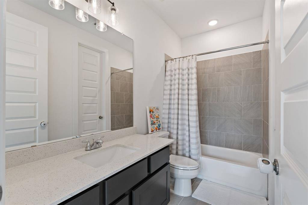 This elegant en-suite bathroom boasts a sleek design with a large mirror, modern lighting, and a spacious vanity with ample storage. The tiled shower and bathtub, combined with a neutral palette, create a clean and inviting ambiance.