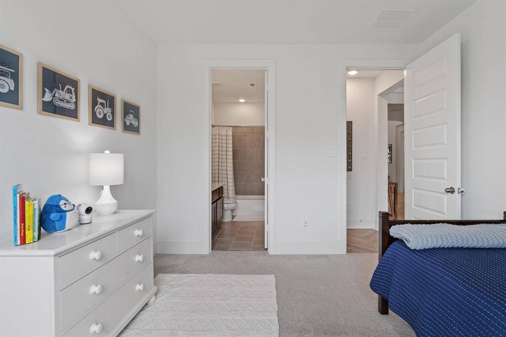 This inviting bedroom features neutral tones, cozy carpeting, and a private bathroom with a stylish tiled shower and tub.