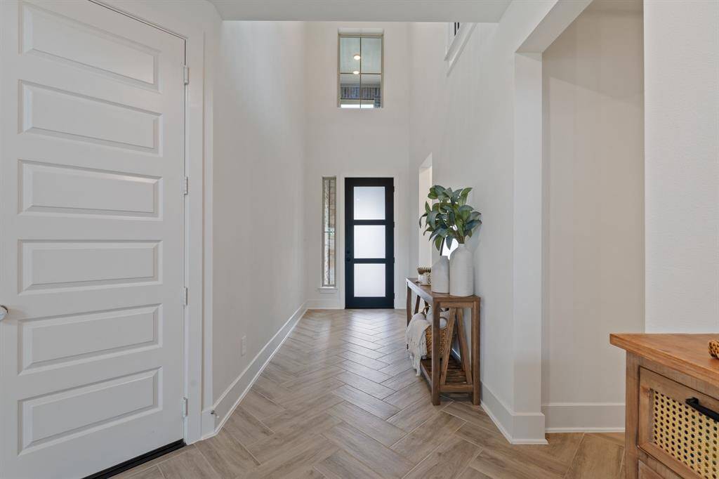 A stunning entryway with high ceilings, modern design, light wood herringbone flooring, and a sleek black front door featuring elegant glass panels.
