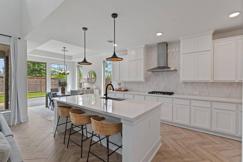 Discover this modern kitchen with sleek white cabinetry, a spacious island with bar seating, and elegant pendant lighting. It seamlessly flows into a bright dining area with large windows and backyard views—perfect for entertaining.