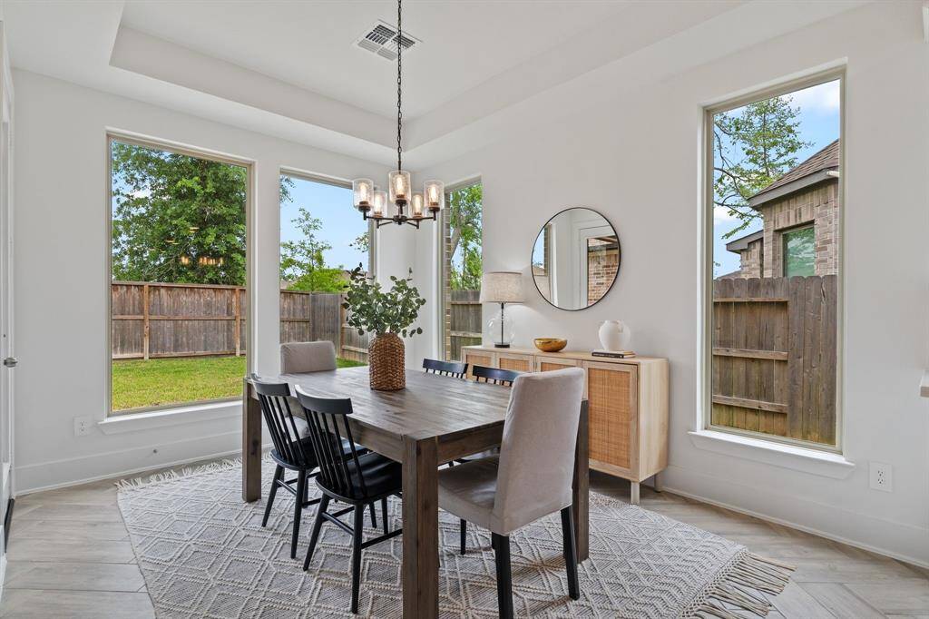 Sunlit dining room with large windows, a modern chandelier, and neutral tones, overlooking the cozy fenced backyard.