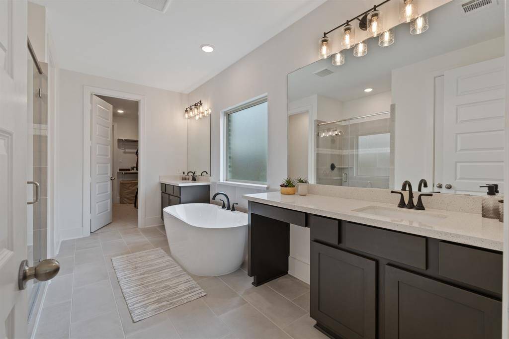 This modern bathroom boasts a spacious design with a freestanding tub, dual sinks with dark cabinetry, and a large mirror. Stylish lighting and a separate shower area enhance its functional design.