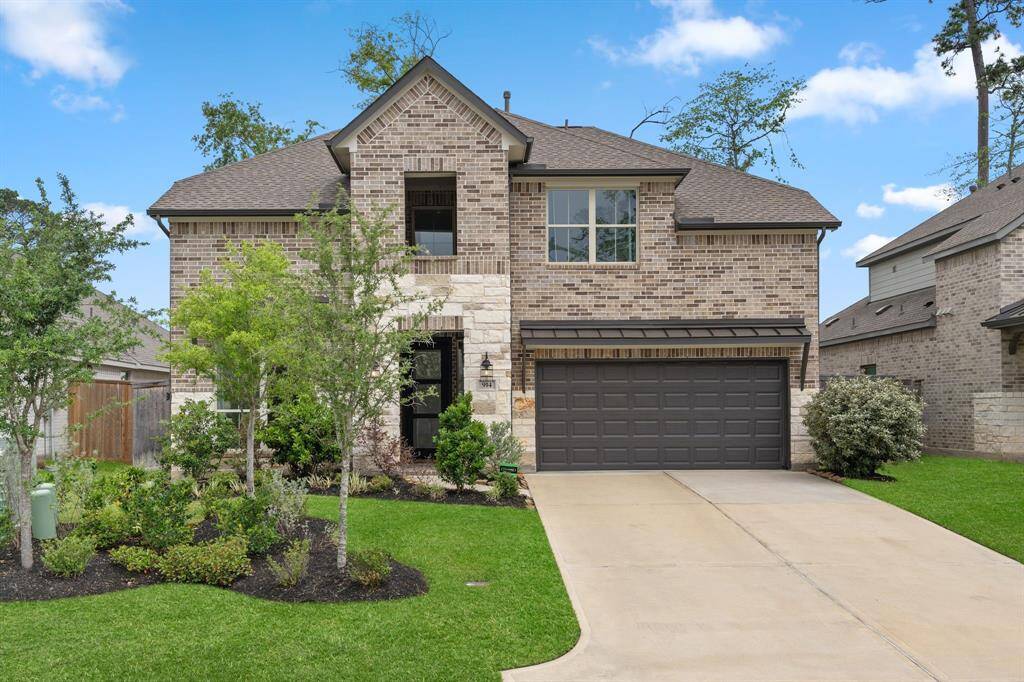 This photo showcases a two-story brick home with a modern design, featuring a two-car garage and a well-maintained front yard with lush greenery and trees. The exterior has a combination of brick and stone accents, giving it a classic yet contemporary appearance.