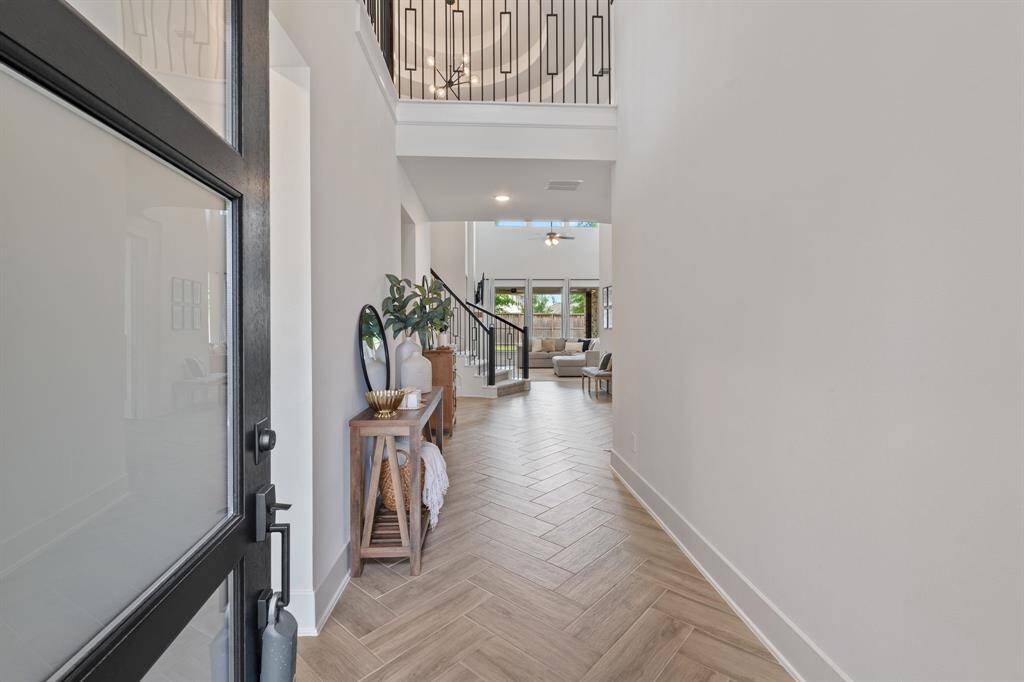Discover a bright, spacious entryway with high ceilings and modern design. Featuring elegant herringbone wood flooring, it opens to a well-lit living area. The stylish open railing staircase leads to the second story.