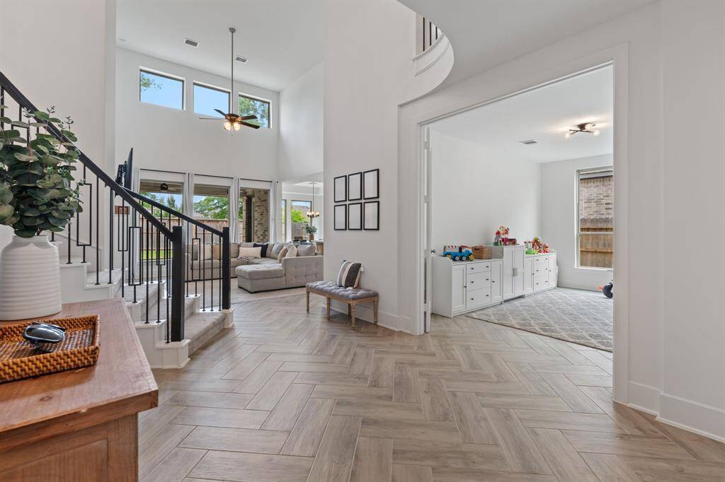 This photo showcases a bright, open-concept living area with high ceilings and large windows, providing ample natural light. The space includes a cozy sitting area, a sleek staircase with modern railings, and a separate flex space.