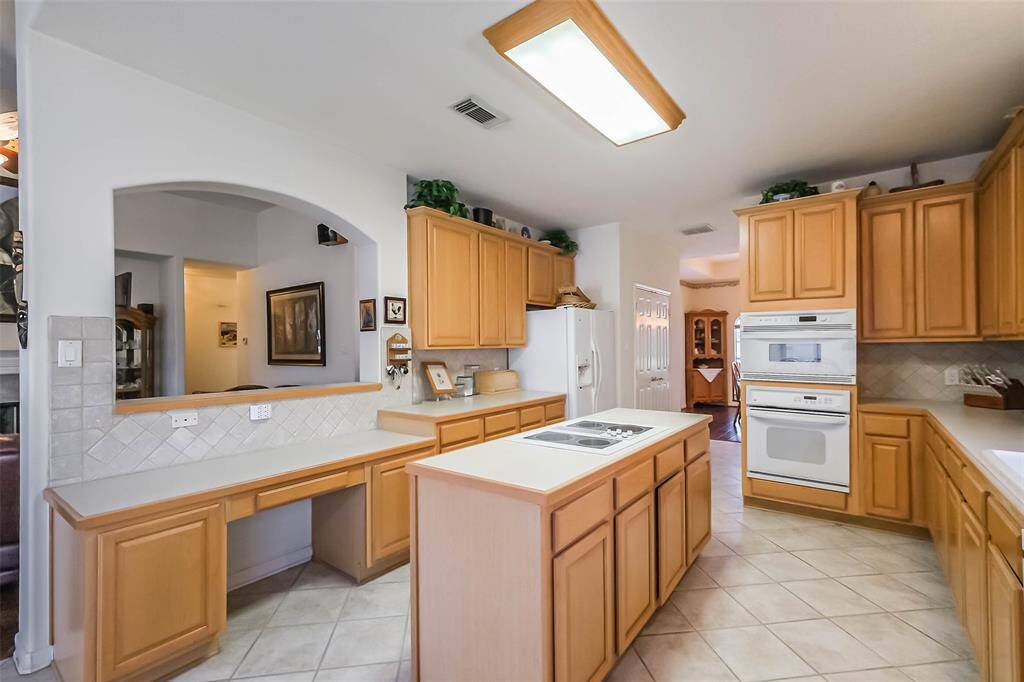This kitchen features ample wooden cabinetry, a central island with a cooktop, tiled flooring, and built-in appliances.