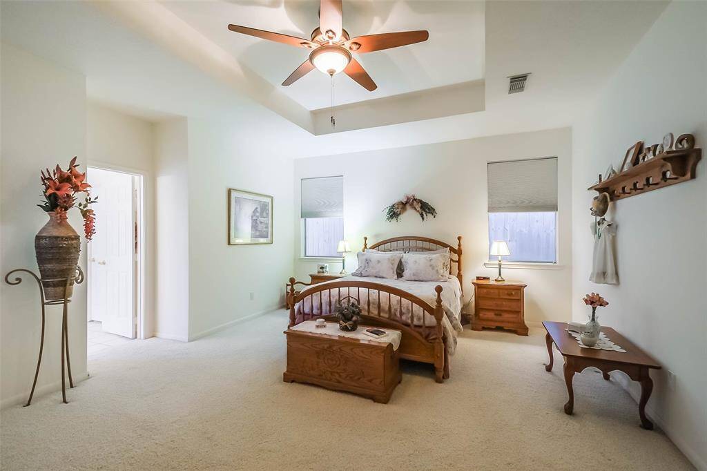 This spacious primary bedroom features an energy efficient ceiling fan, tray ceiling, and soft carpeted flooring. It includes ample natural light from three windows, and a convenient en- suite bathroom entrance.