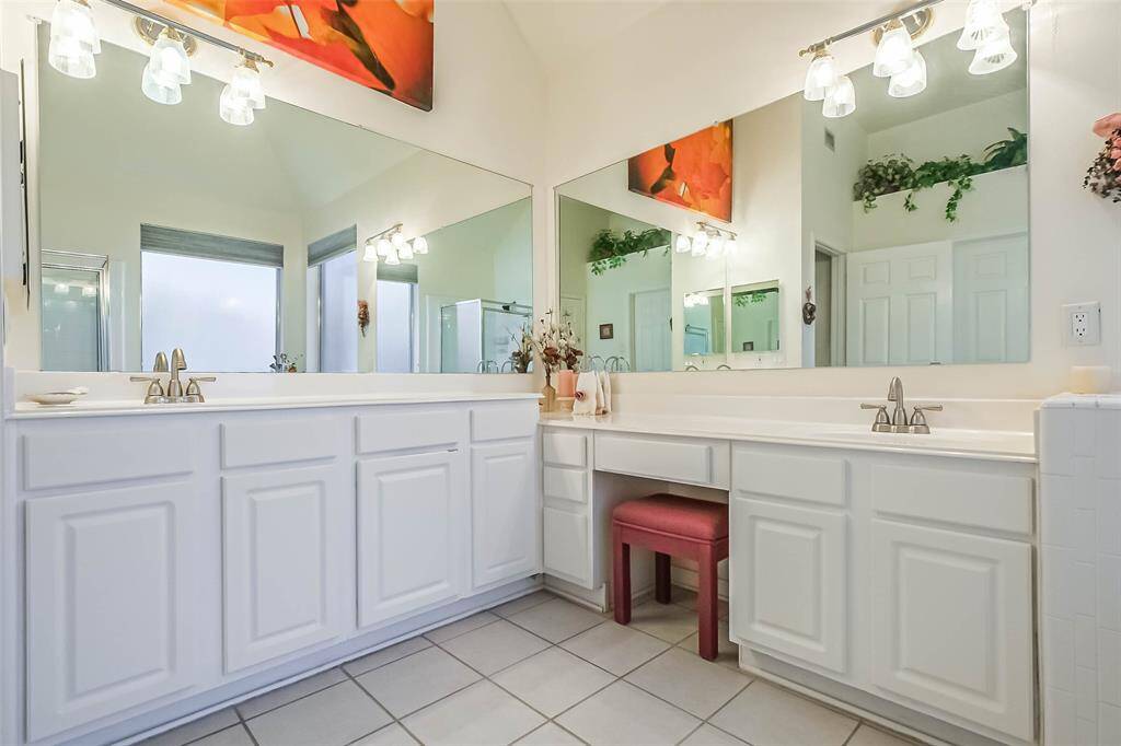 Another view of the primary bathroom showcases dual vanities with ample counter space, large mirrors, and elegant lighting. The white cabinetry adds a clean, classic touch.