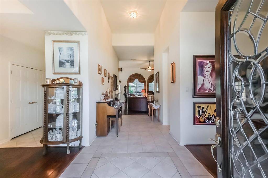 The welcoming foyer with high ceilings and tiled flooring creates space that leads to the well-lit family room with a ceiling fan, adding to the home's inviting ambiance.