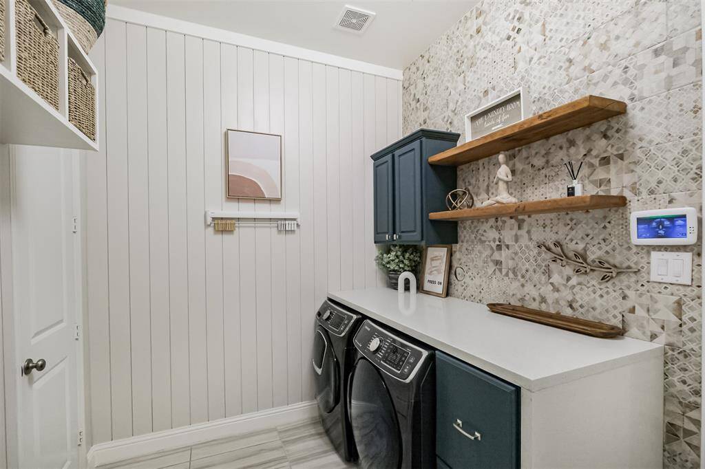 Even the laundry room has been customized! Decorative tile and floating shelves adorn the walls. The cabinet housing the machines provides the ideal folding surface and drawer space for supplies. The door to the left leads to another deep walk-in storage closet.