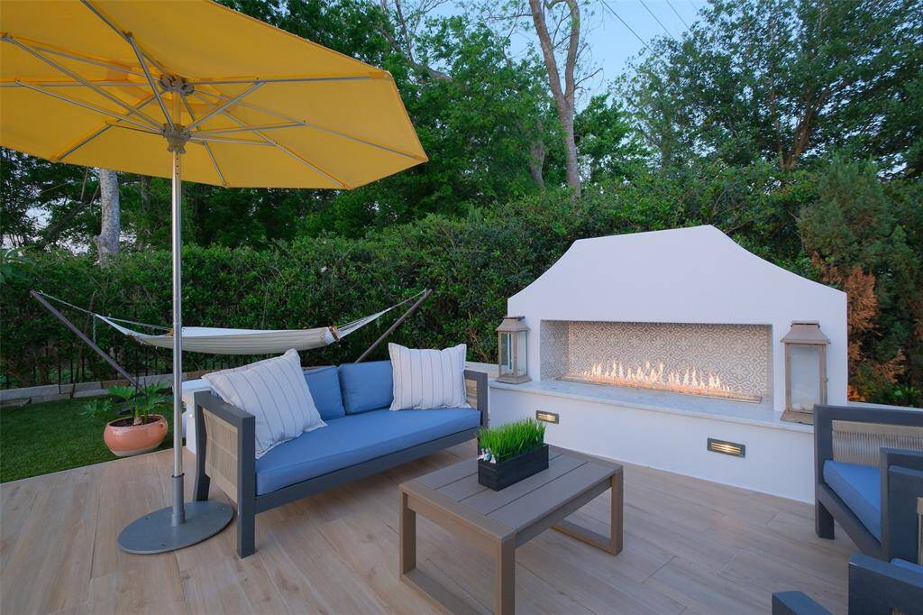 The uncovered section of the back patio is anchored by this stunning white stucco Mediterranean-style, glass rock gas fireplace with custom tile.