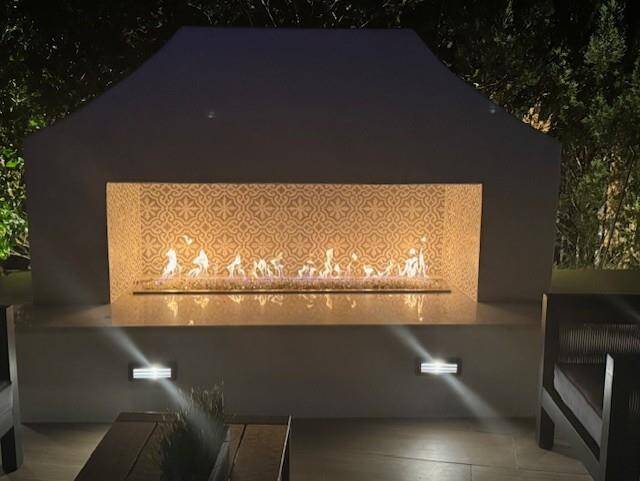 The Mediterranean style fireplace at night with custom tiles highlighted by the glow of the warming flames.