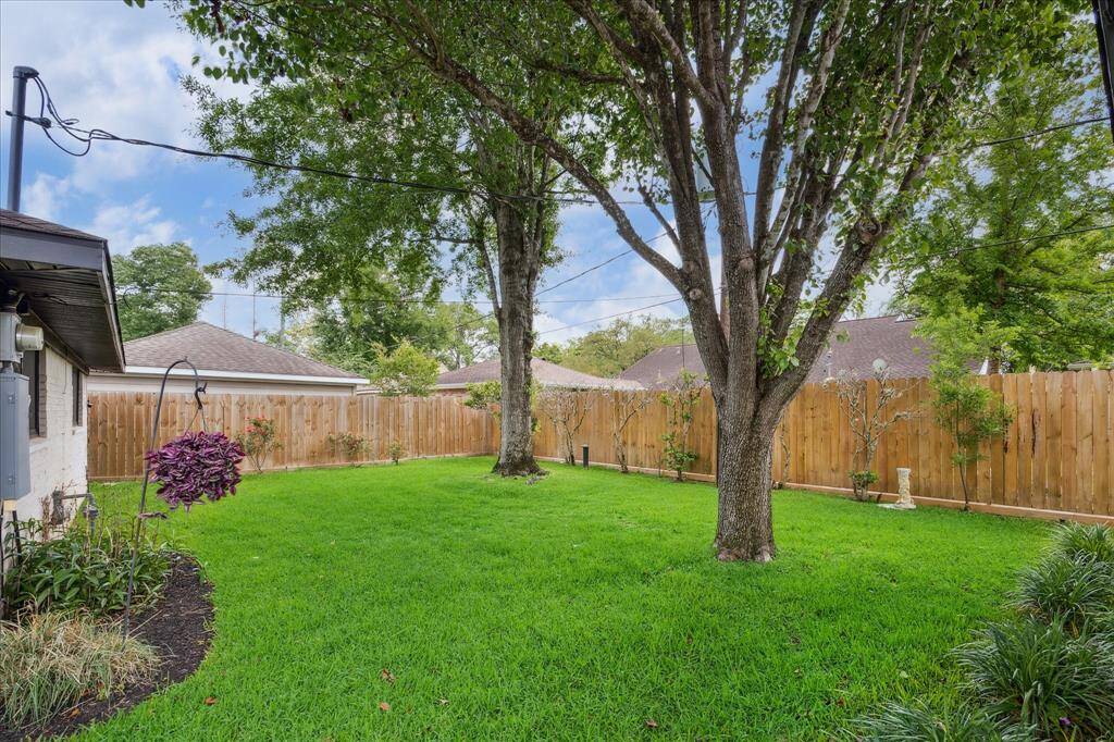 Backyard with grass space, mature trees, lush landscaping and wood privacy fence.