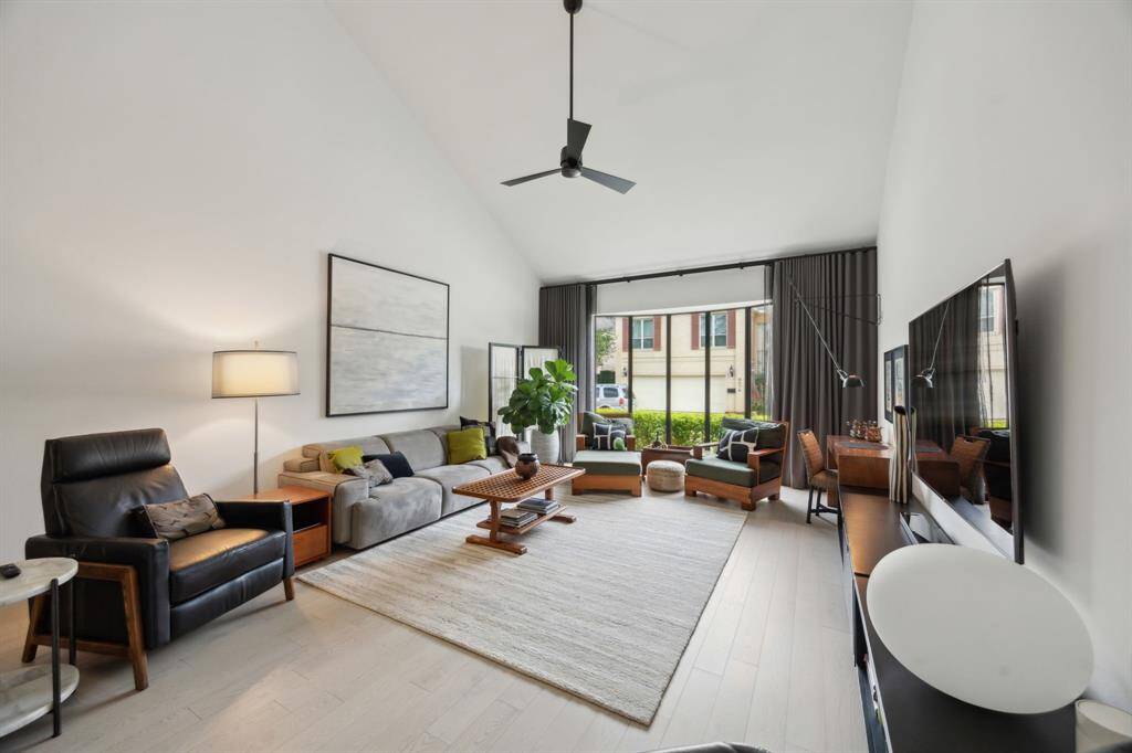 Another view of the living room with ceiling fan and large windows overlooking the front landscape.