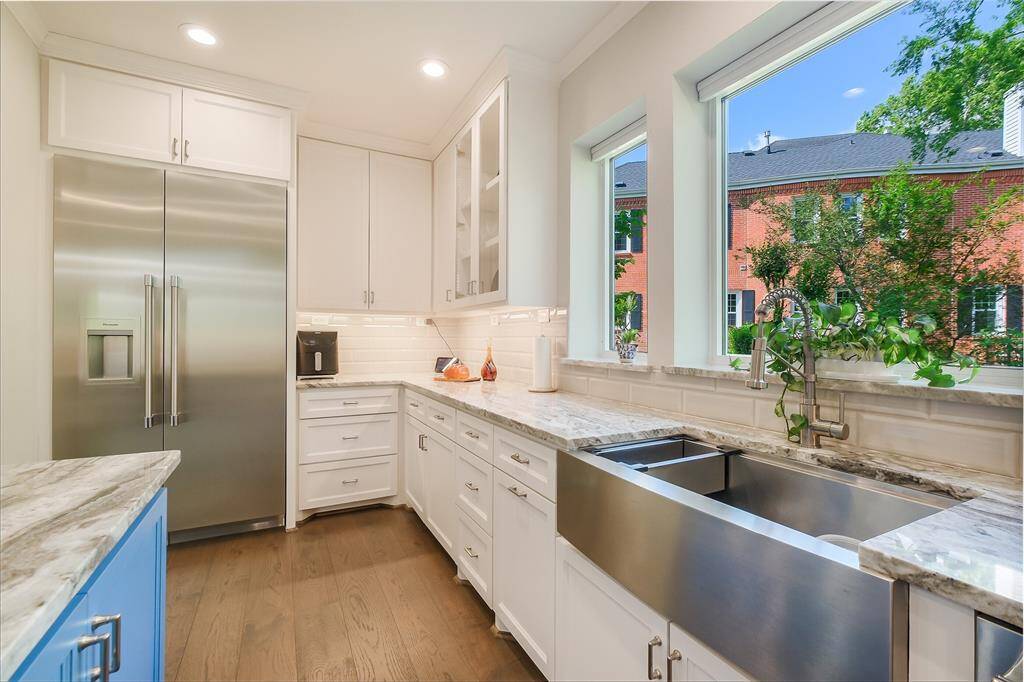 Three oversized picture windows above the sink overlooking a greenbelt, filling the space with natural light. A deep farmhouse sink, glass -front cabinets, and extensive counter space make this kitchen as functional as it is beautiful.