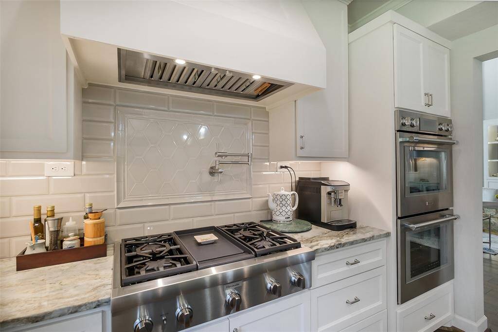 A Thermador range with pot filler is set against beautiful architectural tilework and crowned by a statement hood, while double ovens complete this impeccably designed chef's kitchen.
