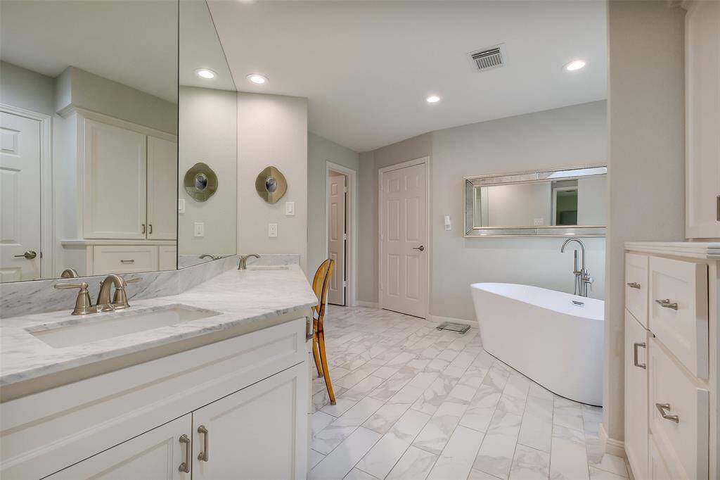Luxurious spa-style bath with elegant marble tile, a spacious dual vanity and two walk-in closets. Thoughtful details include built-in cabinetry for streamlined storage and a modern neutral palette that enhances the serene ambiance.