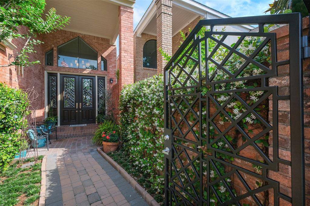 Step through the wrought iron gate into a serene private courtyard with jasmine-covered walls and a striking double front door entry framed by a soaring brick column.