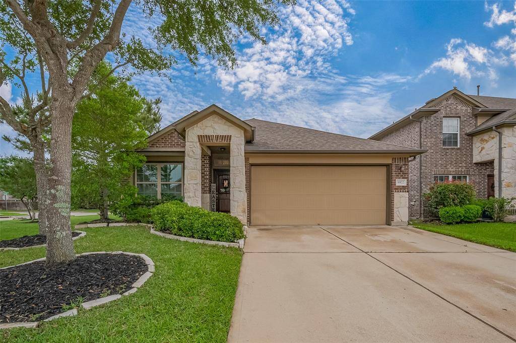 This charming single-story home features a brick and stone exterior with a well-maintained lawn and landscaping. It has a spacious two-car garage and a pleasant front entrance, perfect for comfortable family living.