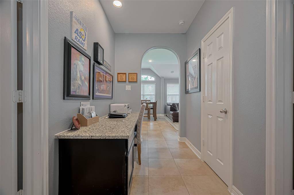 This desk area featuring a granite countertop and tiled flooring, leads to a bright living area with large windows.