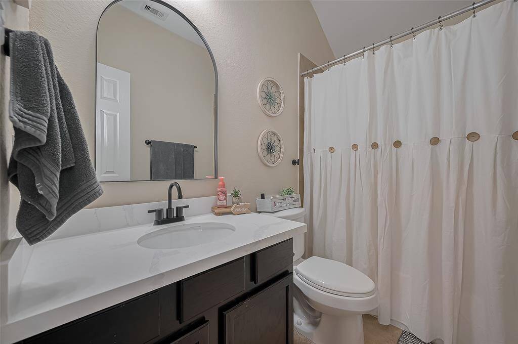 This bathroom features a modern design with a sleek wooden vanity, white countertop, and a stylish arched mirror. It includes a tub/shower combination with neutral walls for a clean, inviting atmosphere.