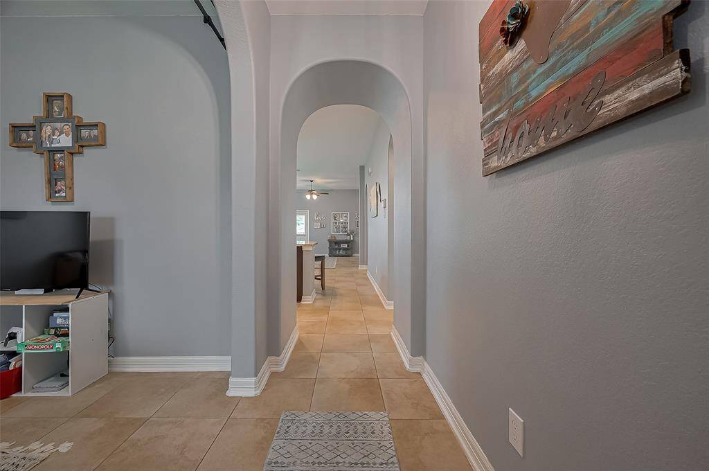 This photo features a bright hallway with light gray walls and tiled floors, leading to aopen living area. The space is accented with arches, creating a cozy and inviting atmosphere.