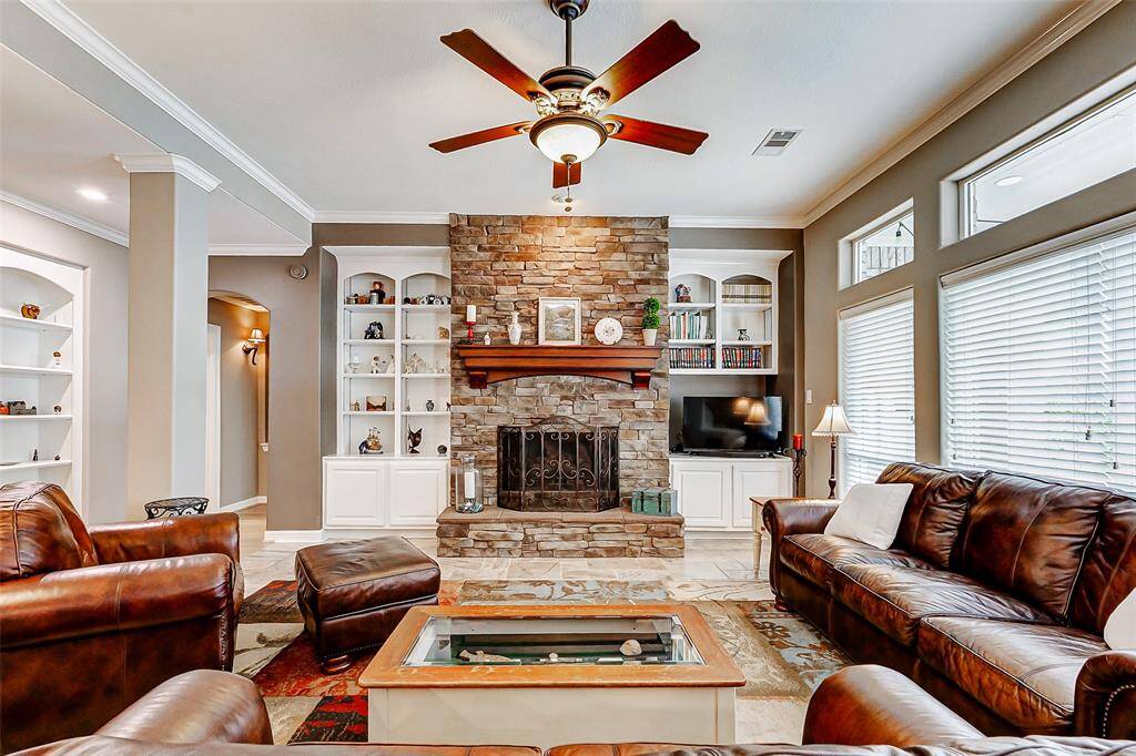 This inviting living room features a cozy stone fireplace, built-in shelving, and ample natural light from large windows.