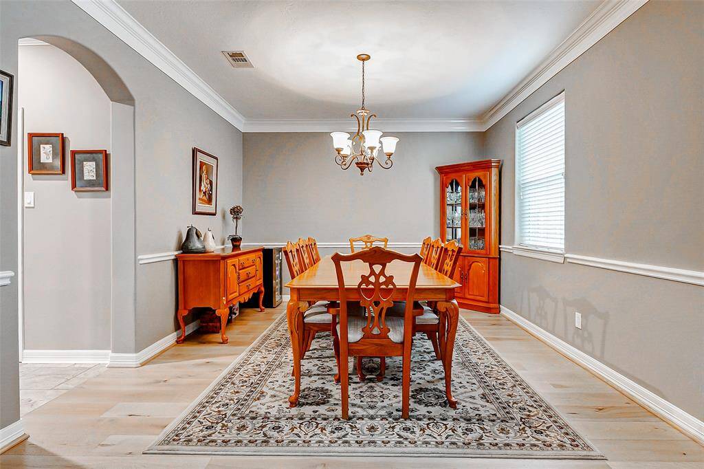 The formal dining room has a neutral color palette, crown molding, and natural light from a large window, creating a warm and inviting atmosphere.