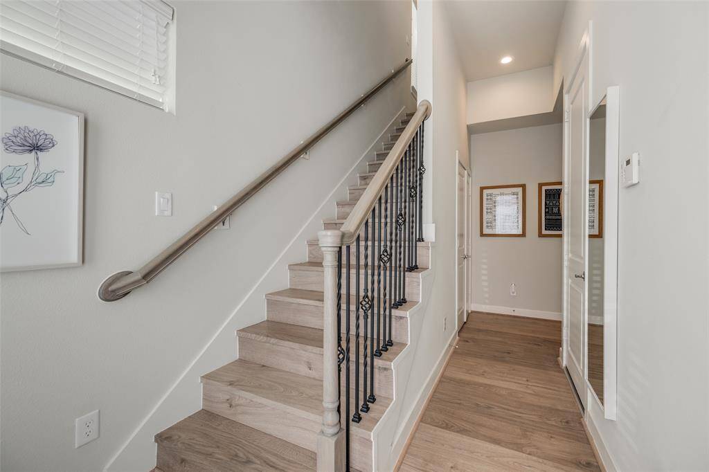 Bright entryway with engineered light hardwood floors, featuring a staircase with beautiful metal rails. A glass door with blinds leads outside, allowing lots of natural light.