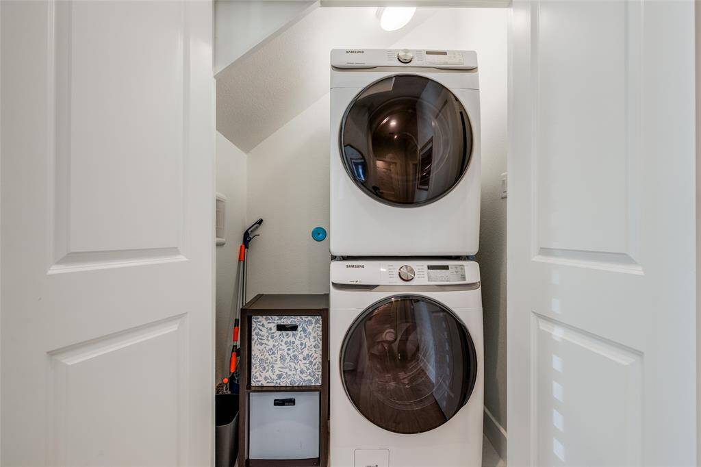 Laundry with stackable front loading modern washer & dryer, space for mops, vacuum & cleaning supplies