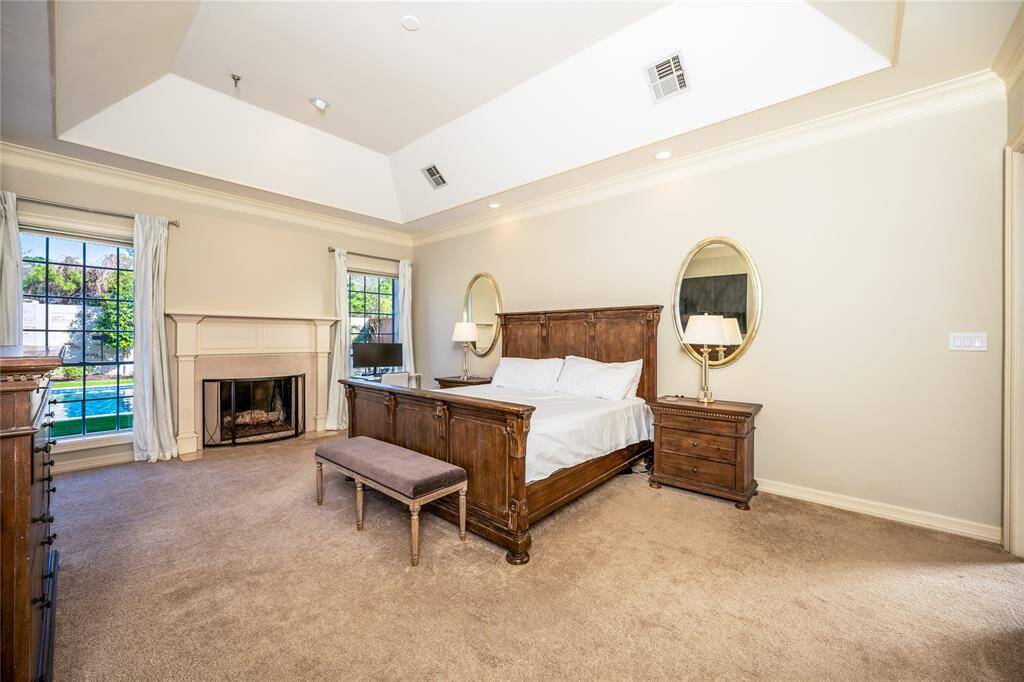 This expansive primary suite exudes timeless elegance, featuring a soaring tray ceiling, a cozy fireplace, and large windows that invite an abundance of natural light, while the refined wood furnishings, plush carpeting.