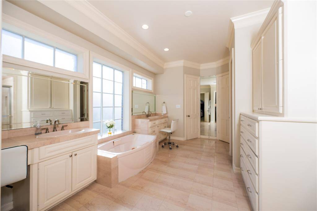 This luxurious primary bathroom boasts dual vanities for added convenience, a spacious soaking tub positioned beneath large windows.