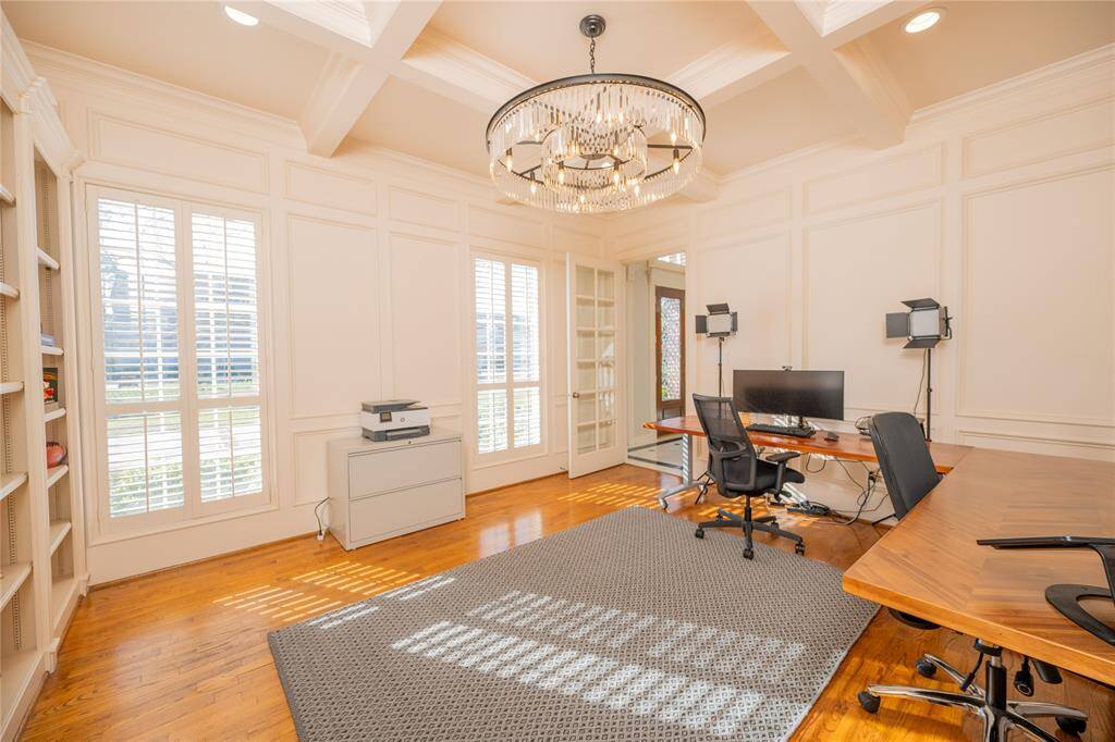 This sophisticated home office features custom-built shelving, rich hardwood flooring, and elegant wainscoting, all illuminated by a statement chandelier.