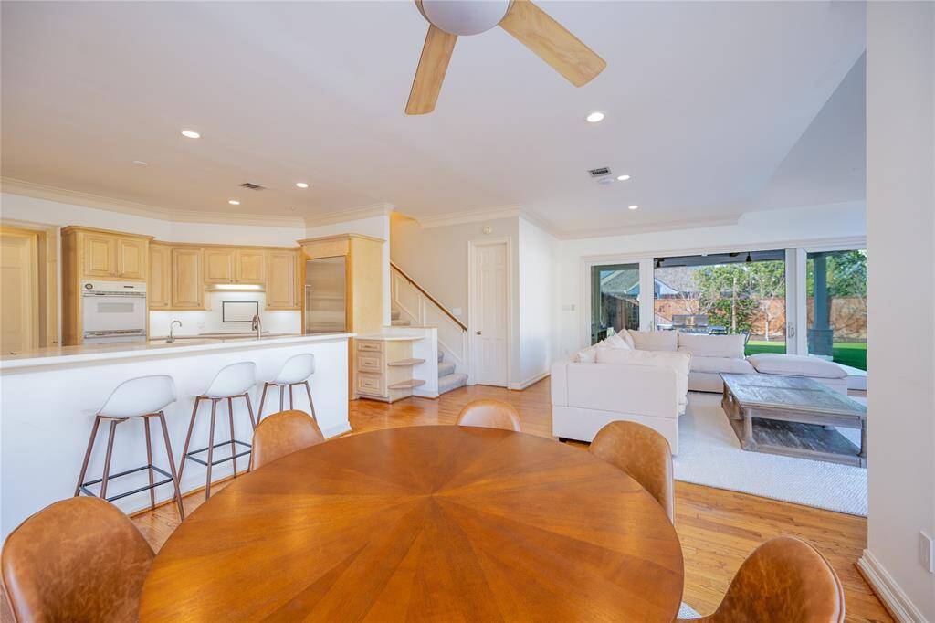 This open-concept living space showcases a beautifully crafted breakfast table, a sleek bar seating area, and a spacious living room, all bathed in natural light from expansive windows that offer stunning views of the lush backyard.