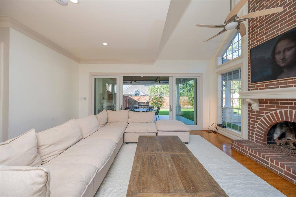 This stunning living room boasts a spacious open-concept design, featuring a cozy gas fireplace with an elegant brick surround, a sleek ceiling fan for added comfort, abundant natural light streaming through large windows and sliding glass doors.