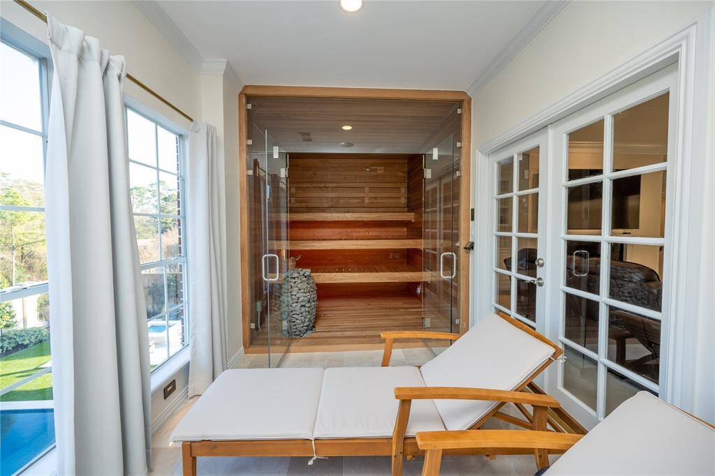 This luxurious private spa retreat features a sleek glass-enclosed sauna with rich wood paneling, ambient lighting, and a premium stone heater, seamlessly connected to a serene relaxation area with plush cushioned loungers.
