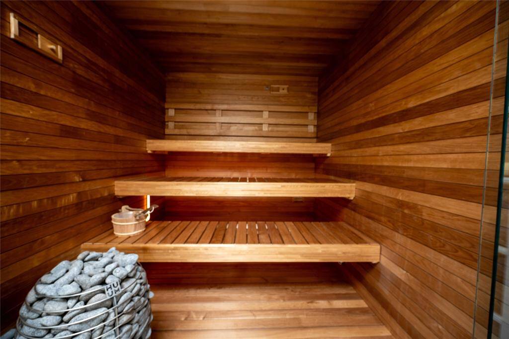This beautifully crafted sauna offers a luxurious spa-like experience, featuring rich, warm-toned wood paneling, multi-tiered bench seating, soft ambient lighting, and a premium stone heater.