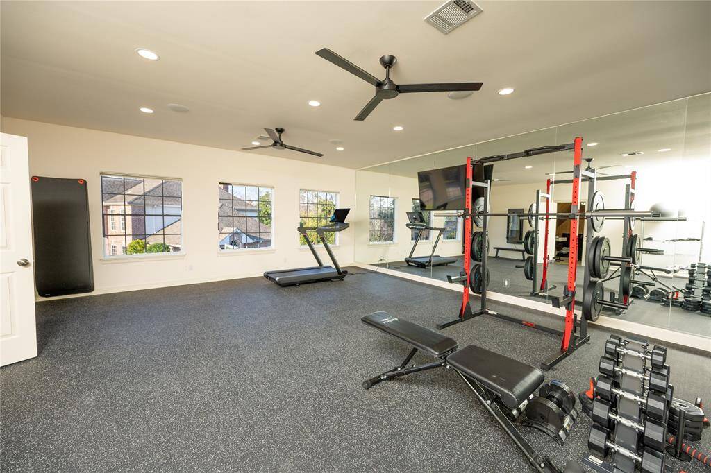 This state-of-the-art home gym offers a spacious and well-lit environment with sleek rubber flooring, a full wall of mirrors, high-performance fitness equipment, and large windows for natural light.