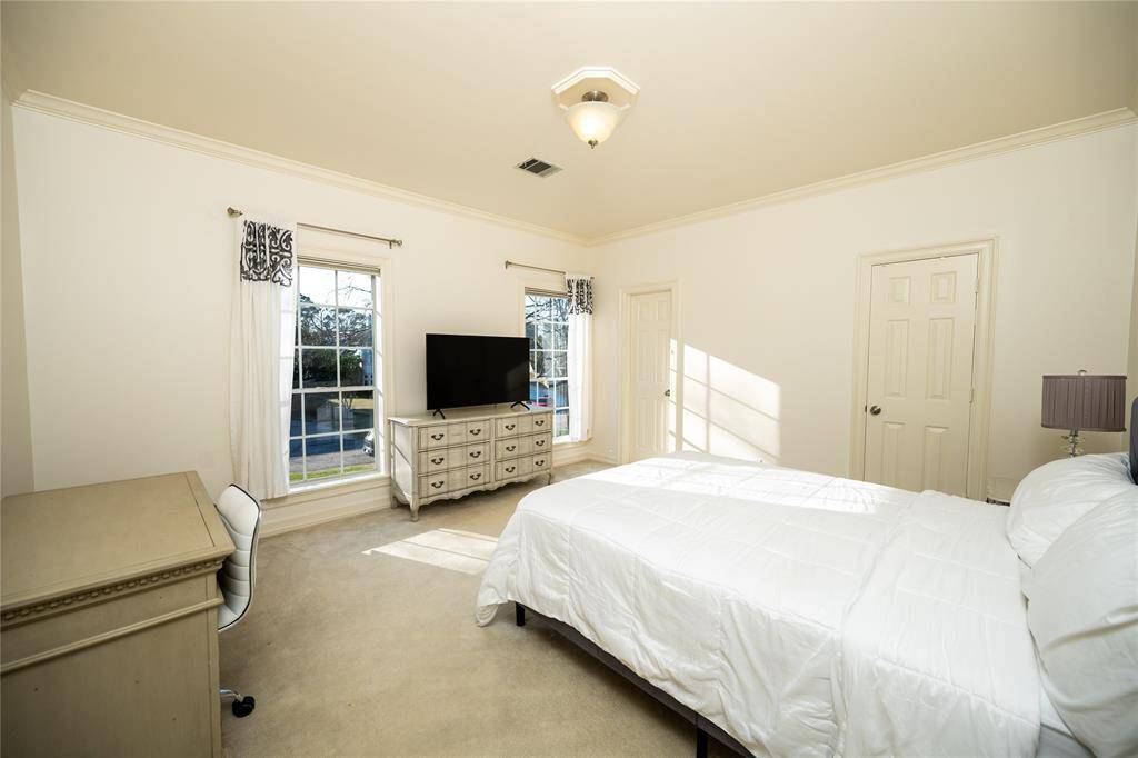 This spacious and serene bedroom is bathed in natural light from large, beautifully framed windows, highlighting the neutral color palette.