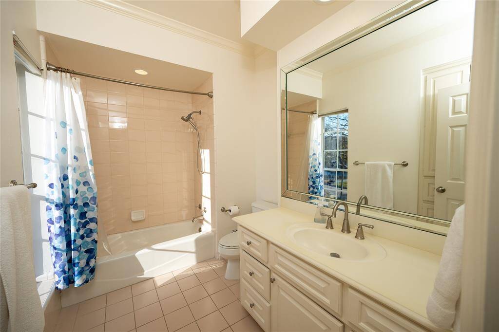 This beautifully designed bathroom features a spacious vanity with ample storage, an expansive mirror that enhances the natural light, and elegant tile flooring that complements the pristine bathtub and shower combination.