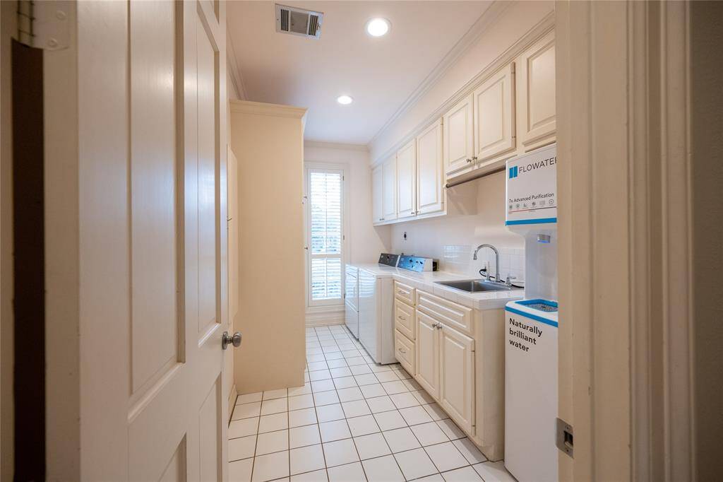 This spacious and well-appointed utility room features abundant cabinetry for ample storage, complemented by generous counter space.